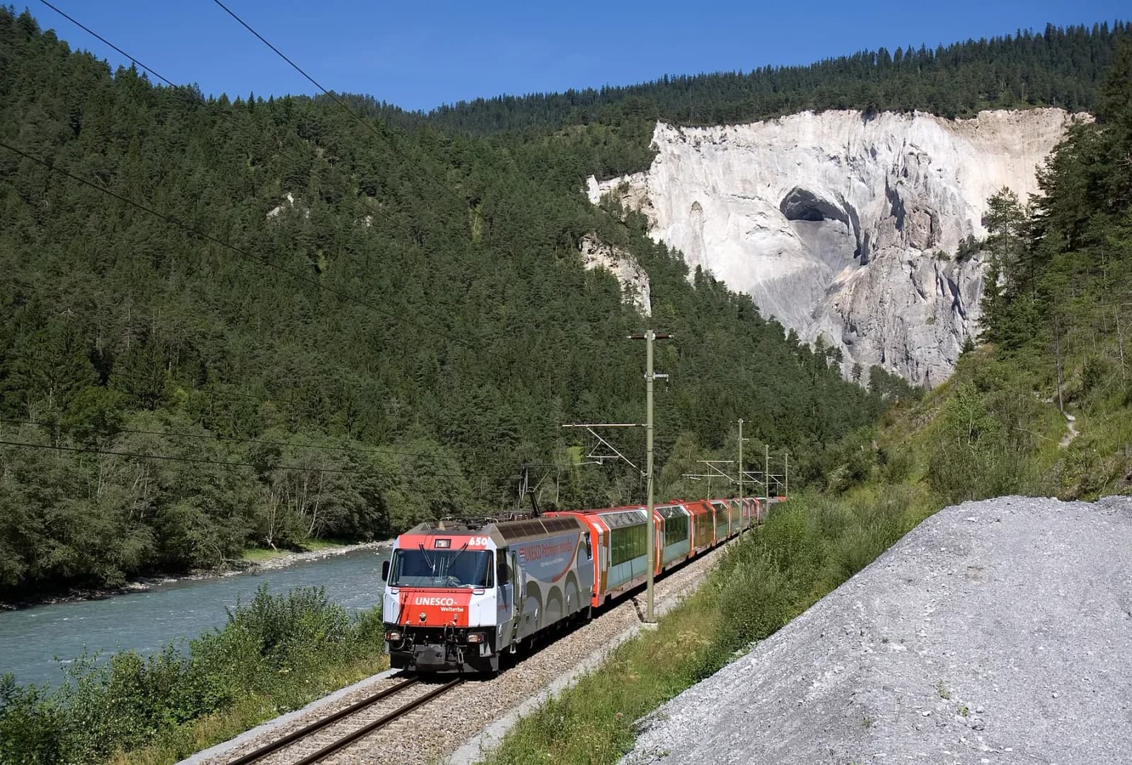 Two red Glacier Express trainsets following the Rhine through a pale-walled gorge