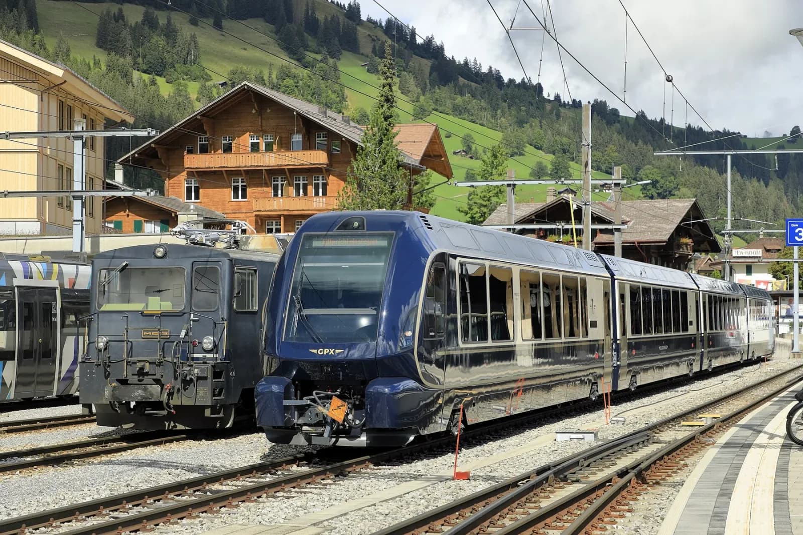 A blue and gold GoldenPass Express standing beside mountain chalets at Zweisimmen