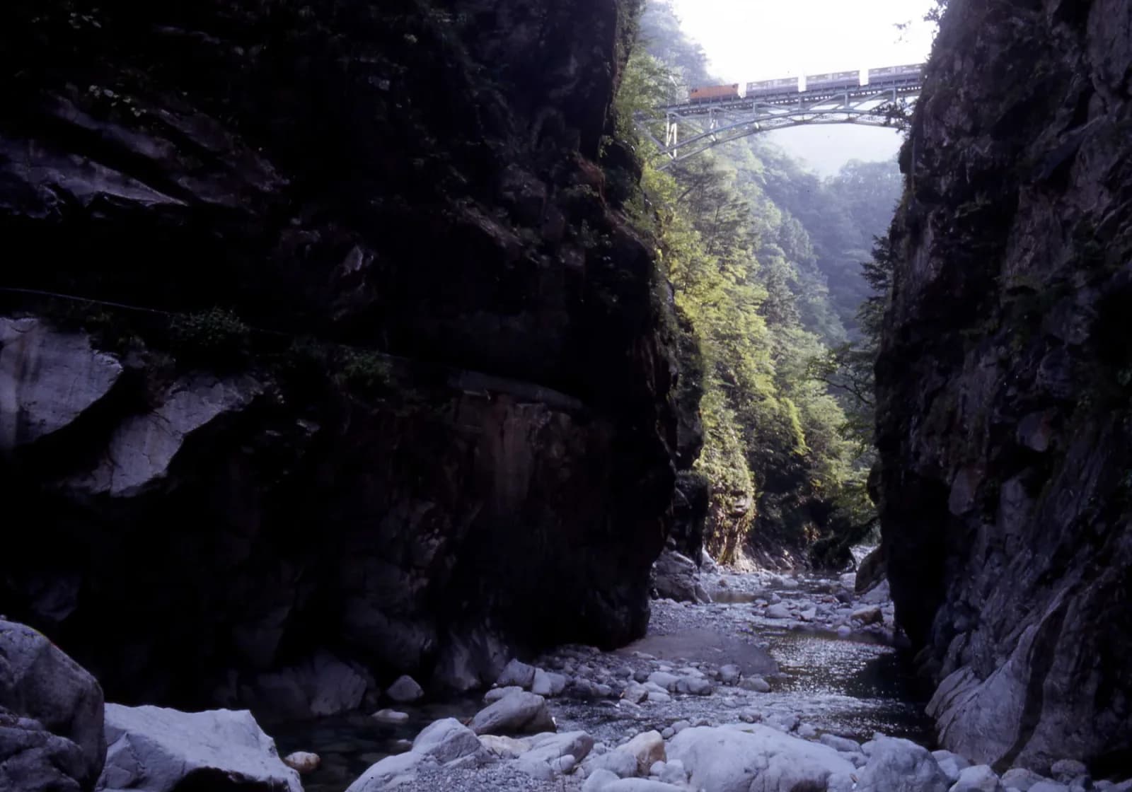 A small Kurobe Gorge Railway train crossing Atobiki Bridge above dense mountain forest
